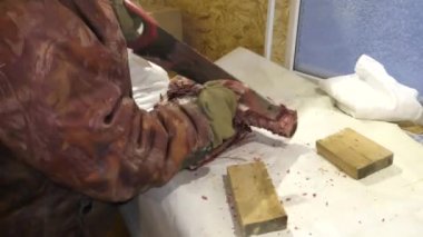 Adamın biri donmuş geyik leşini kesiyor.