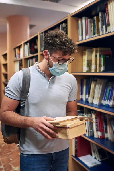 man with a mask is reading books in the university library