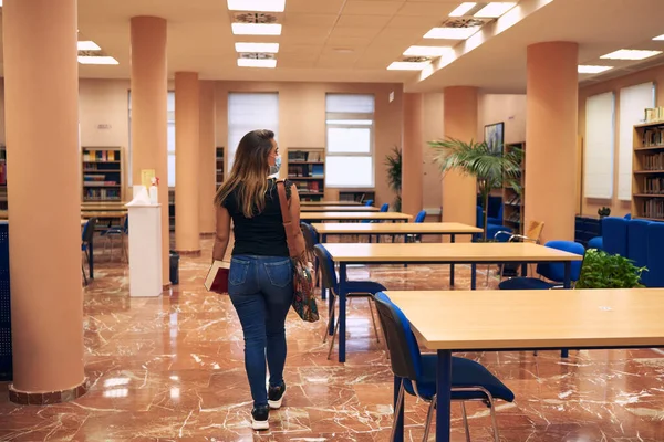 Maskeli ve sırt çantalı kız boş bir kütüphaneye giriyor.