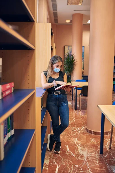 Una Ragazza Con Una Maschera Piedi Biblioteca Guardare Libro — Foto Stock
