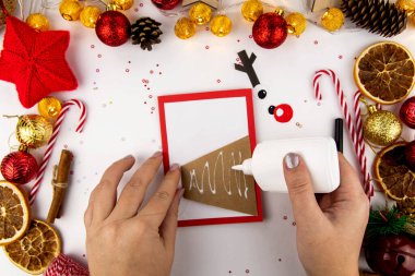 Çocuklu bir Noel kartı için adım adım talimatlar. Renkli kağıt, yapıştırıcı ve makasla yapılmış bir kartpostalda Noel geyiği. 4. Adım.