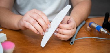 Kadın manikürü evde kendisi yapıyor. Kadın ellerine yakın çekim. Kadın eski verniği bir dosyayla temizliyor..