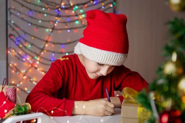 Kırmızı Noel şapkalı çocuk Noel Baba 'ya mektup yazıyor.