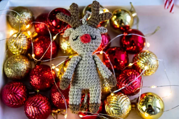 Handmade crocheted deer on the background of Christmas balls and garland lights.