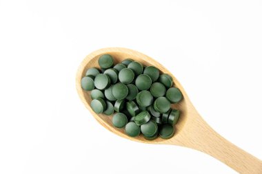 Beyaz arka planda tahta kaşıkta yeşil spirulina hapları. Boşluğu kopyala.