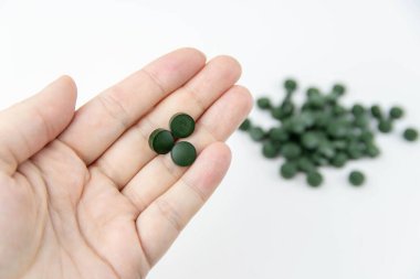 Bir kadının elinde üç yeşil hap, vitamin sarmalı ve bulanık yeşil haplar var..