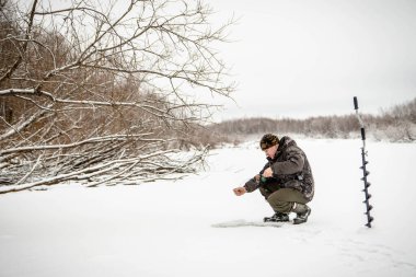 Kışın balık. Bir adam kışın bir deliğin yanındaki buzda oturur ve küçük bir olta kamışı tutar. Bir balıkçı kışın balık tutar.