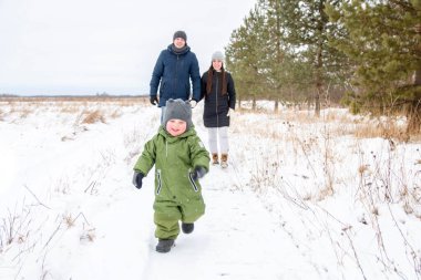 Neşeli çocuk kışın kar altında koşar ve ailesi onu takip eder. Aile kışın yürür