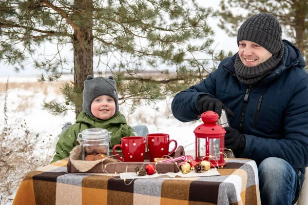 Winter picnic in the woods. Dad and son sit at the table and drink hot tea from the thermos