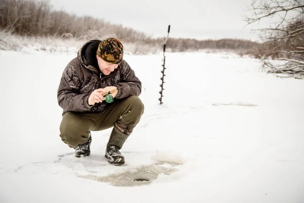 Winter fishing. A man sits on the ice next to a hole in winter and holds a small fishing rod. A fisherman fishs in winter