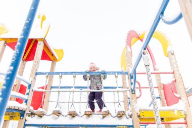 Neşeli kız kışın oyun alanında oynar. Kız asma köprüde yürüyor..
