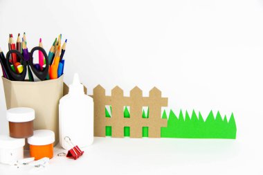 Renkli kalemler, yapıştırıcılar, boyalar, çimenler ve renkli kağıtlardan oluşan beyaz bir masa manzarası. Çocukların yaratıcılığı kavramı.