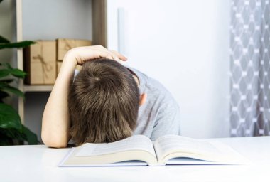 Okullu çocuğun oğlu açık bir kitapta kafasını masaya koydu. Öğrenci kavramı okumak, öğrenmek istemez.