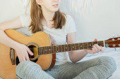 Mladá dívka v bílém tričku sedí a hraje na akustickou kytaru