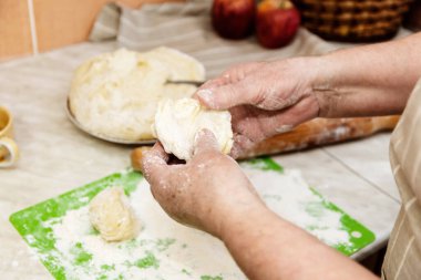 Ev koşullarında pişirme kavramı. Yaşlı kadının ellerine yakın plan hamur yoğurur.
