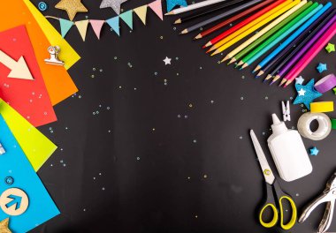 Bright colorful background with colored pencils, paper, scissors, glue for children's creativity on a black table. Space to copy