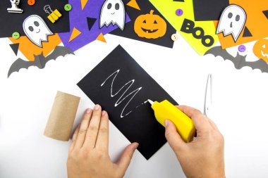 Bir çocukla Cadılar Bayramı 'nda tuvalet kağıdı ruloları ve siyah kağıt yarasadan maharet. Adım adım talimatlar.