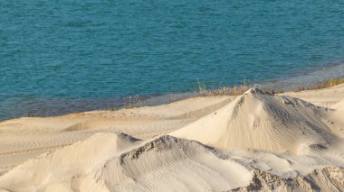 Sarı kum tepeleri ve mavi su doğal çöl arazisi. Taş ocağının dalgalı deseni