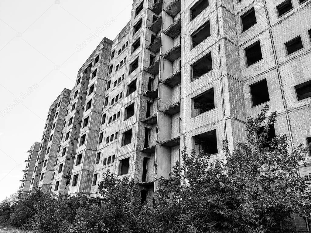 High multistorey abandoned soviet building facade with crashed balconies in black and white. Weathered housing estate, unfinished city of nuclear scientists in Birky, Ukraine