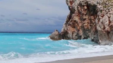 Yunanistan 'ın Lefkada adasının sahilindeki kayalık kayalıklara vuran gök mavisi parlak ve kuvvetli dalgalar. Yazın İyon Denizi 'ne vahşi doğa yolculuğu