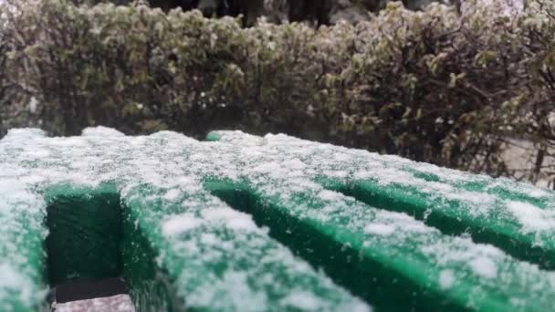 雪のフレーク市内公園 冬のクローズアップでゆっくりと緑のベンチに落ちています 光の背景季節のスローモーション映像 — ストック動画