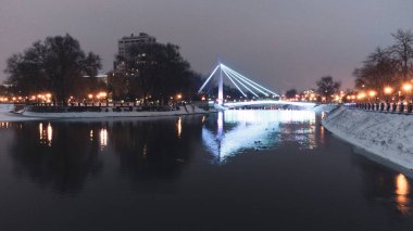 Köprü (Mist Zakokhanykh) Kharkiv şehir merkezinde, aydınlatılmış Skver Strilka 'da nehir boyunca uzanır. Kış havası akşam rengi fotoğrafında su yansıması var.