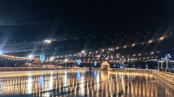 Ukrayna 'nın Kharkiv kenti Karazina Üniversitesi (Kharkiv) yakınlarındaki Svobody Meydanı' nda açık ayna yansıtıcı yüzey ve aydınlatma ışıkları üzerinde kimsenin olmadığı kış gecesi buz pateni pisti