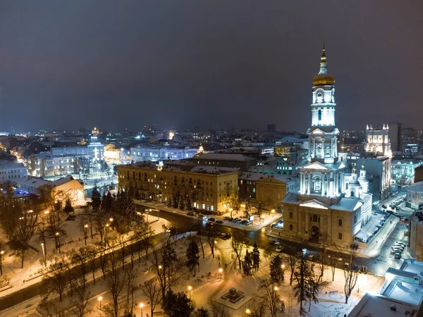 Kışın karlı akşam ışıklarıyla aydınlatılan Dormition Katedrali. Ukrayna şehir merkezindeki Kharkiv havacılık manzaralı.
