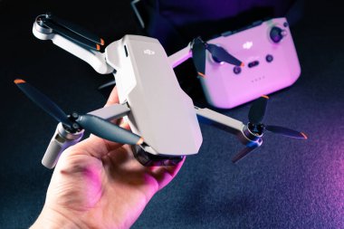 Kiev, Ukrayna - 02 Şubat 2021: Dji Mavic Mini 2 insansız hava aracı. Açılan kuadkopterle el ele tutuşup mor ışıkta siyah arkaplan üzerinde uzaktan kumanda kuracağız.