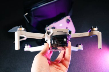 Kiev, Ukraine - February 02, 2021: Dji Mavic Mini 2 drone close-up. Hand holding unfolded quadcopter with remote control on black background in purple light clipart