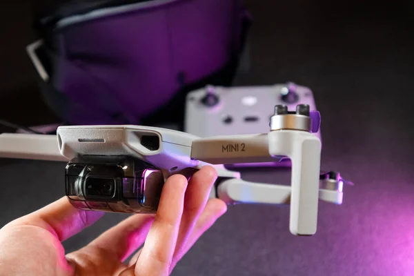 Kiev, Ukrayna - 02 Şubat 2021: Dji Mavic Mini 2 insansız hava aracı. Açılan kuadkopterle el ele tutuşup mor ışıkta siyah arkaplan üzerinde uzaktan kumanda kuracağız.