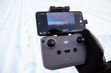 Kharkiv, Ukrayna - 21 Şubat 2021: Dji Maviç Mini 2 (dji air 2) uzaktan kumandalı uzaktan kumanda ile bağlı telefon arayüzü ile kış eldivenleri. Beyaz kar arkaplanında İHA çalıştırılıyor