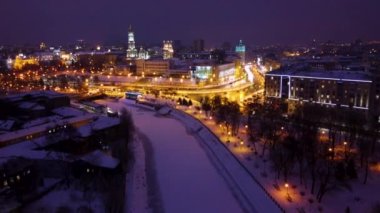 Kış akşamı, işlek arabalarla trafik ve donmuş karlı nehirlerle aydınlık şehir hava görüntülerini hızlandırır. Skver Strilka, Dormition Katedrali, Serhiivskyi Meydan, Harkiv, Ukrayna