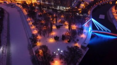 Aydınlatılmış bir akşamın üzerinde uçan Skver Strilka, Harkiv şehir merkezinde karla kaplıydı. Kış akşamı renkli video 4k