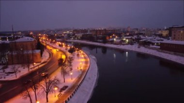 Kharkiv şehir merkezinde, karanlık sularda ışık yansıması ve yakınlarda giden arabalarla aydınlık akşam nehrinin üzerinde hız artırımı yapmak. Kış akşamı renkli video 4k