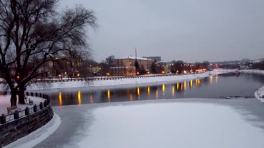 Lopan Nehri ve Harkiv kavşağı setinin su yüzeyinin üzerinden alçak uçun. Şehir ışıkları suya yansıyor. Kış karlı hava şehir merkezi