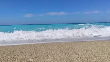 Yunanistan 'ın Lefkada adasının açık mavi sularıyla çakıl taşı plajında beyaz fırtınalı dalgalar yaklaşıyor. Yaz vahşi doğa seyahati İyon Denizi 'ne