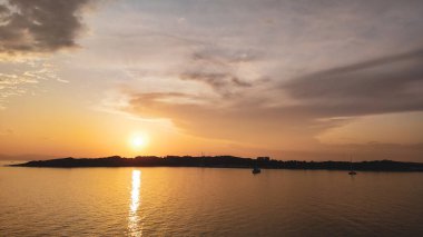 Yunanistan 'da Atina yakınlarındaki Ege Denizi' ndeki Yunan adalarının üzerinde parlayan turuncu günbatımı güneşi. Yaz turizmi. Akşamları sakin denizde manzara bulutları ve yatlar
