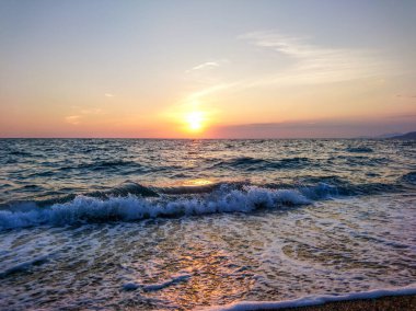 Güzel beyaz dalgalarla deniz kıyısında parlayan turuncu günbatımı güneşi. Yaz denizi huzurlu seyahati, Yunanistan 'da akşam