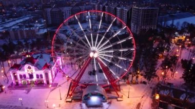 Aydınlatılmış dönme dolaba yakın hava görüntüsü. Kışları Kharkiv şehir merkezinde insansız hava aracı görüntüleri. Gün batımında eğlence Gorky Central Park. Şehir ışıkları, sokaklar şehir manzarası ufuk çizgisi