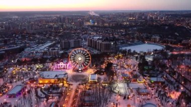 Dönme dolapta hava manzarası. İnsansız hava aracı Kharkiv şehir merkezinde daireler çizerek uçuyor. Gün batımında eğlence Gorky Central Park. Şehir ışıkları, sokaklar şehir manzarası ufuk çizgisi