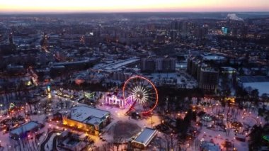 Dönme dolapta hava manzarası. Kışları Kharkiv şehir merkezinde İHA sağa doğru uçar. Gün batımında eğlence Gorky Central Park. Şehir ışıkları, sokaklar şehir manzarası ufuk çizgisi