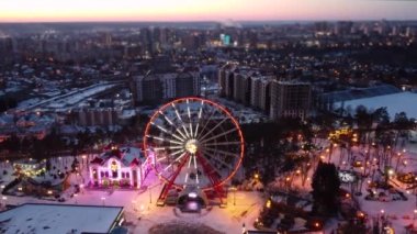 Dönme dolapta hava manzarası. Kışları Kharkiv şehir merkezinde İHA soldan sağa uçuyor. Gün batımında eğlence Gorky Central Park. Şehir ışıkları, bulanık efektli sokaklar