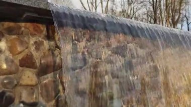 Şehir parkında gün batımında parlayan taştan duvarla birlikte akan temiz kaynak süslemeli su taşması. Şehir Parkı Çeşmesi