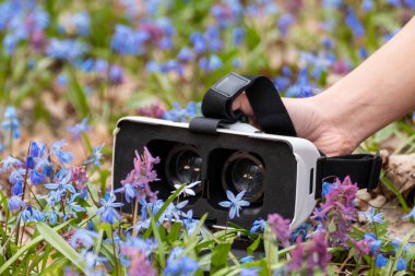 3D sanal gerçeklik gözlüğü, bahar mavisi ve mor yabani çiçeklerle açılmış lensler. VR teknik ekipman gözlükleri yakın plan. Akıllı telefonlar için optik sistem