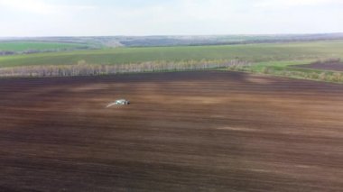 Mavi traktörün ekili araziye tohumları püskürterek sağa sürüşünü gösteren hava manzarası. Tarım ilkbahar kırsal arazisi
