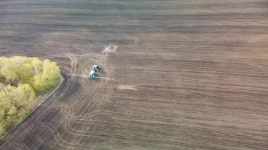 Mavi traktörün tarlaya doğru döndüğü ve püskürdüğü hava görüntüleri. Tarım tarım ilkbahar ekipmanları