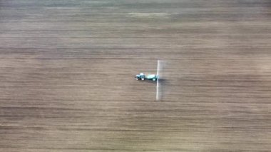 Sola doğru giden ve ekilmiş tarlalara tohum sıkan mavi traktörlü hava aracı. Tarım ve baharın arka plan görüntüleri. Yan görünüm