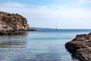 Kayalık kayalıklar kıyısı olan vahşi Akdeniz, uzaklarda yelkenli tekne ve mavi berrak su. Atina yakınlarında Yunanistan 'ı gezmek. Yaz doğası manzaralı göl