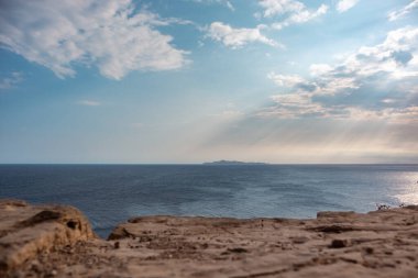 Yunanistan 'ın kayalık kıyılarında bulutların üzerinde parlayan güneş ışınları. Akdeniz su yüzeyinde dramatik bulut manzarası